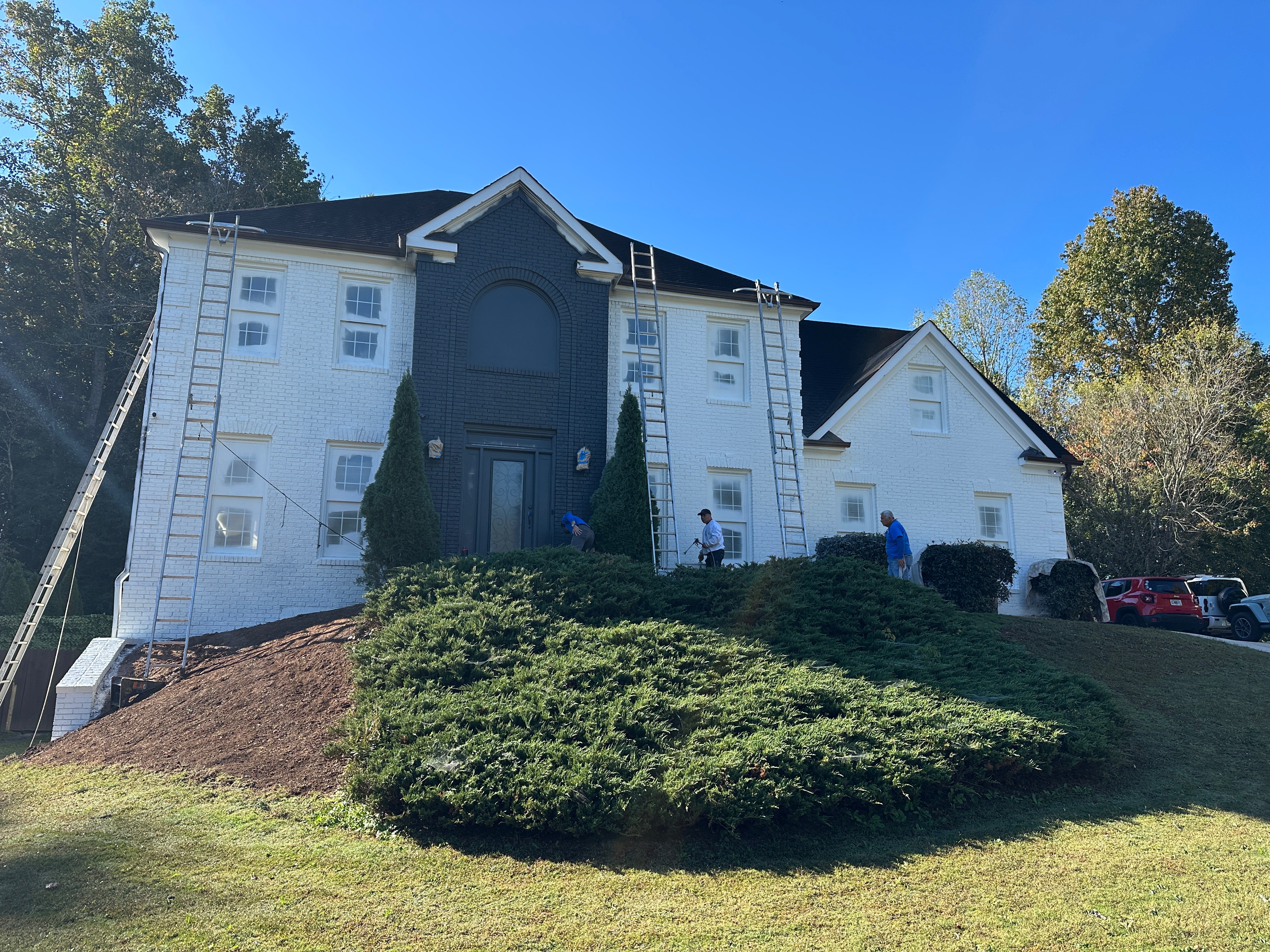 Crew painting white brick two-story home with multiple ladders